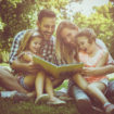 Happy family with two children   in meadow reading book together.