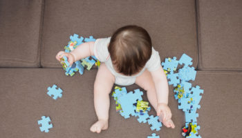 Baby boy playing with puzzle pieces on sofa in the living room at home